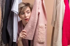 Saleswoman peeking out from behind clothes rack