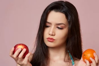 Young woman choosing between an apple and an orange