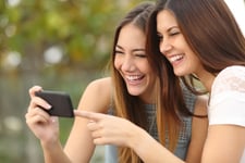 Two smiling young women watching videos on phone