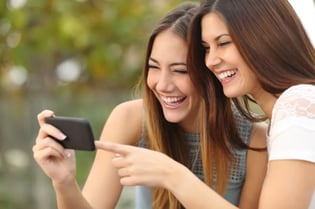 Two smiling young women watching videos on phone