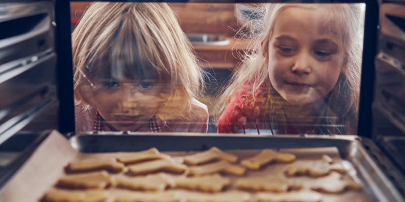 Two girls watching cookies bake 