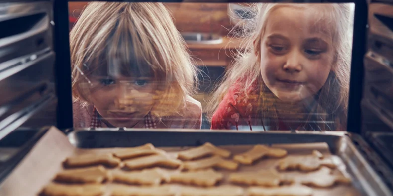 Two girls watching cookies bake